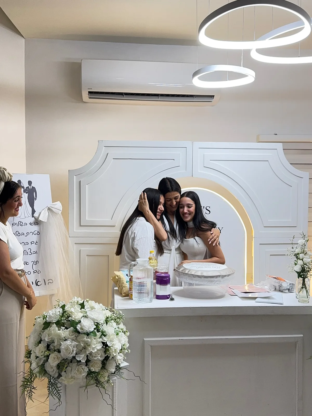 כלה מתחבקת עם חברותיה בערב הפרשת חלה, פרחים לבנים ועיצוב עדין